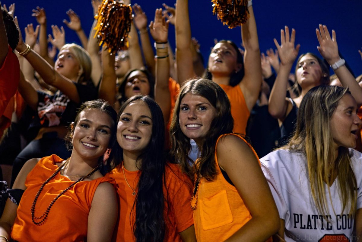 Seniors Finley Kasner, Grier Brown, and Haley Barlow pose for a photo while students in background get excited for the game 