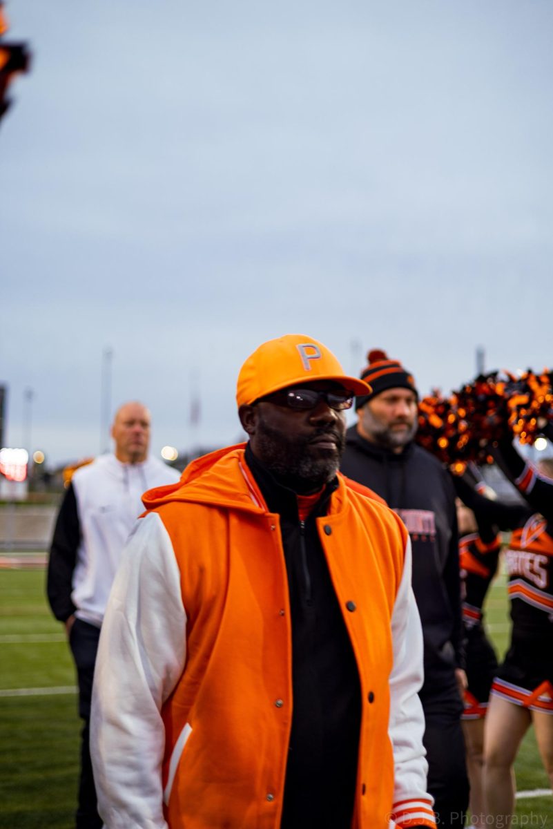 Coming in behind the football players, Assistant Coach Wayne Baskerville walks in down the aisle formed by the cheerleaders 